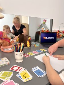 Zajęcia logopedyczne w Akademii LOOK w Katowicach – terapeuta pracuje z dzieckiem przy stole pełnym kolorowych pomocy dydaktycznych i kart